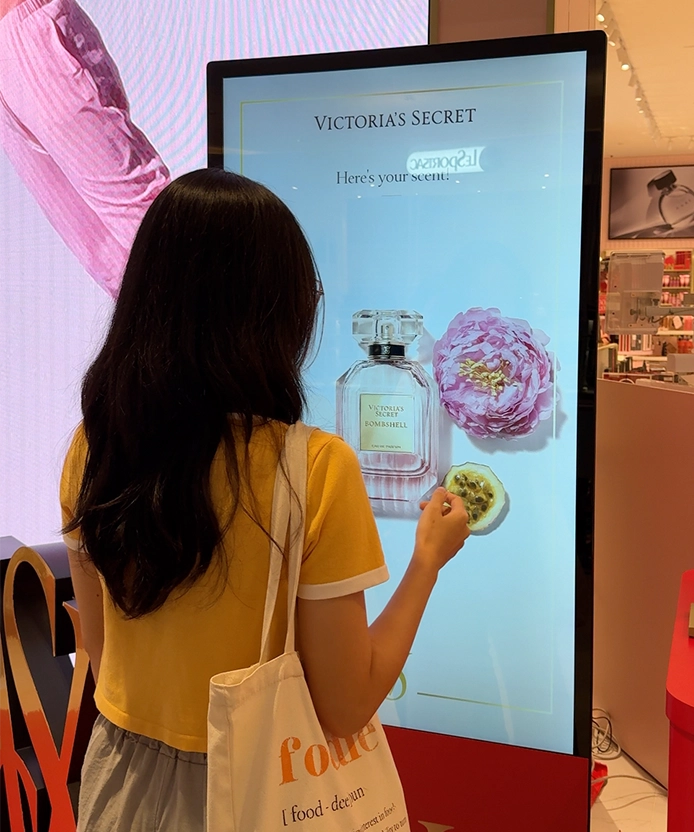Customer using the Victoria's Secret scent-finder kiosk recommending Bombshell fragrance with peony artwork