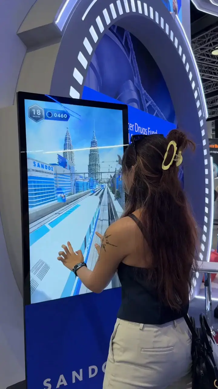 Visitor playing the Sandoz interactive train game on the touchscreen kiosk, with a Kuala Lumpur skyline and score timer on screen