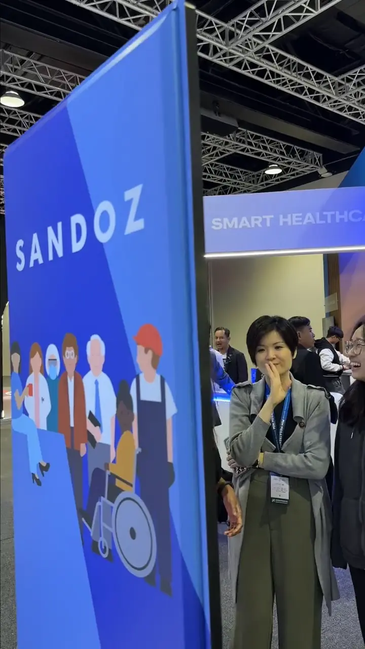 Expo visitors beside the Sandoz pillar featuring illustrated patients and healthcare workers at the Smart Healthcare booth