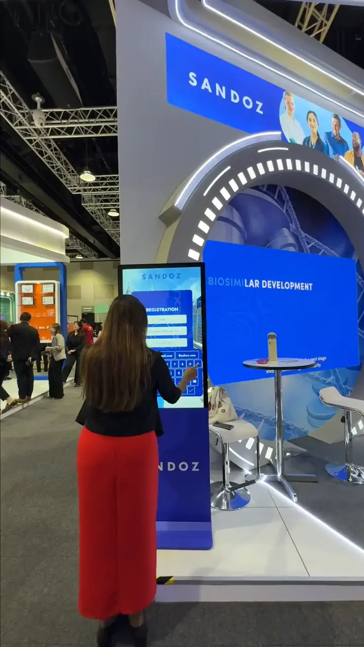Attendee filling in the registration form on the Sandoz touchscreen kiosk in front of the "Biosimilar Development" display wall