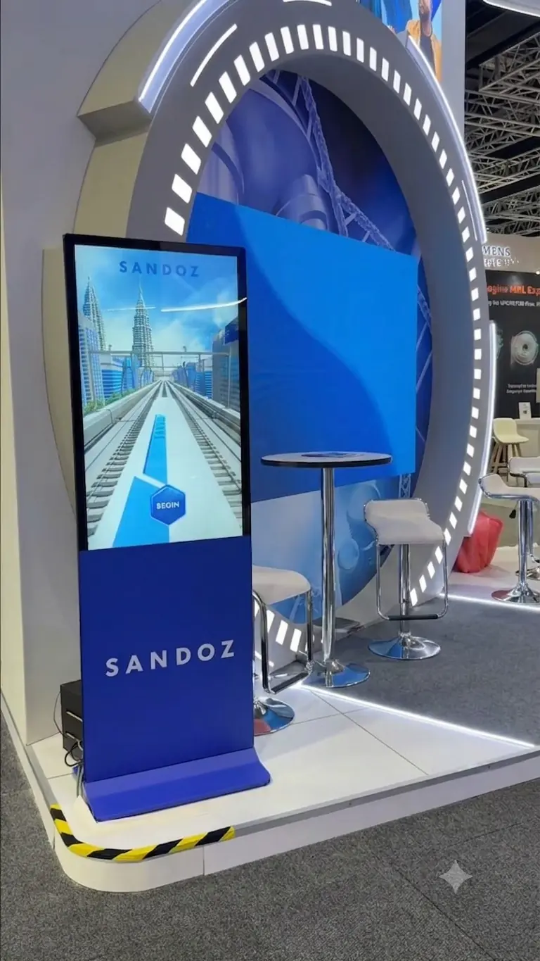 Sandoz booth's interactive train-game touchscreen kiosk on its "Begin" start screen, set under a backlit circular archway with bar seating