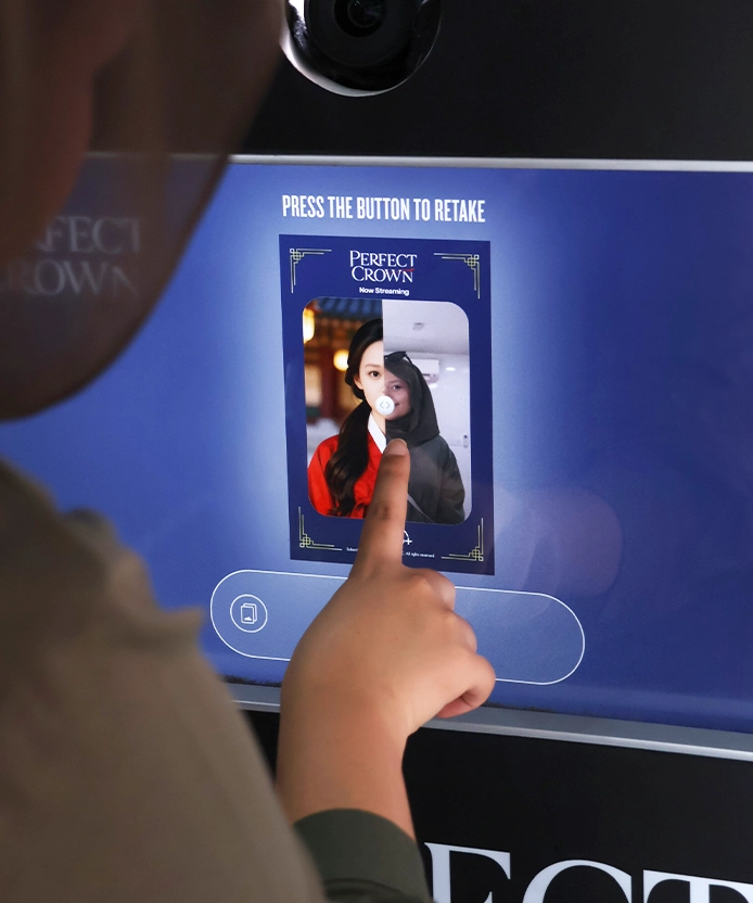 Visitor tapping the booth's touchscreen, showing her photo mid-transformation in a Perfect Crown frame.