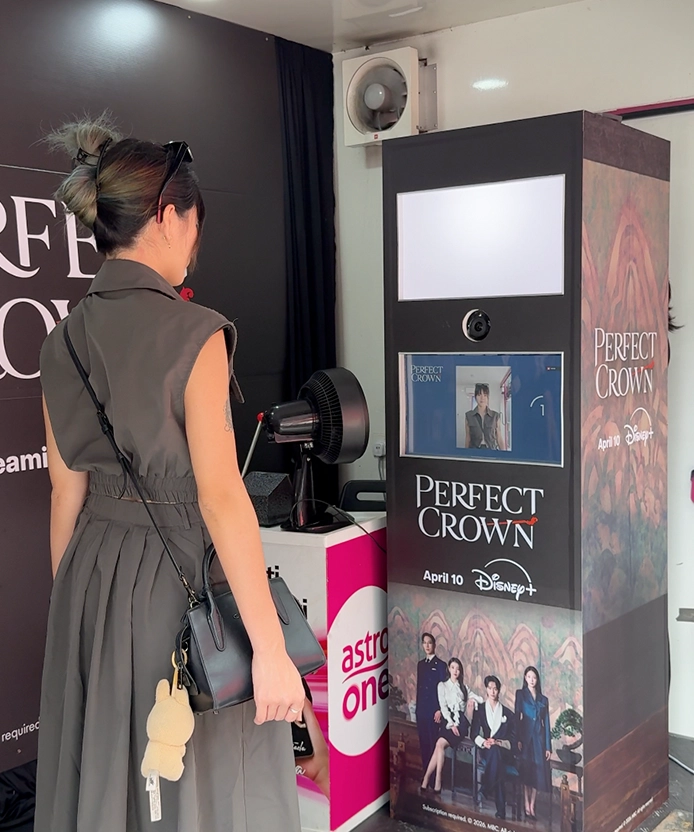 Visitor standing in front of the Perfect Crown photo booth, ready to take her photo.