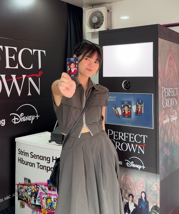 Smiling visitor holding up her Perfect Crown photo card in front of the booth.