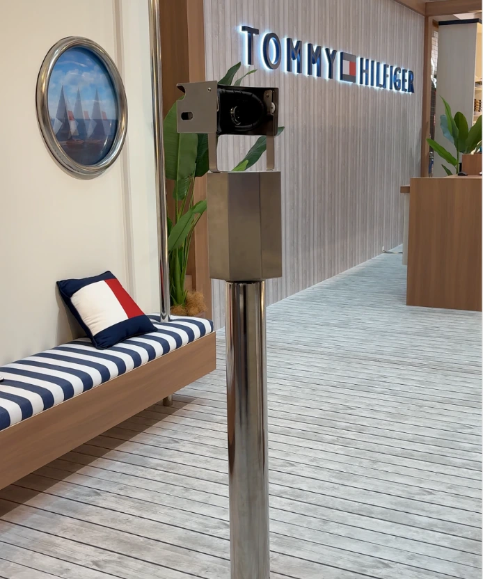 Metal viewfinder on a chrome pole in front of the Tommy Hilfiger store, with a nautical striped bench nearby