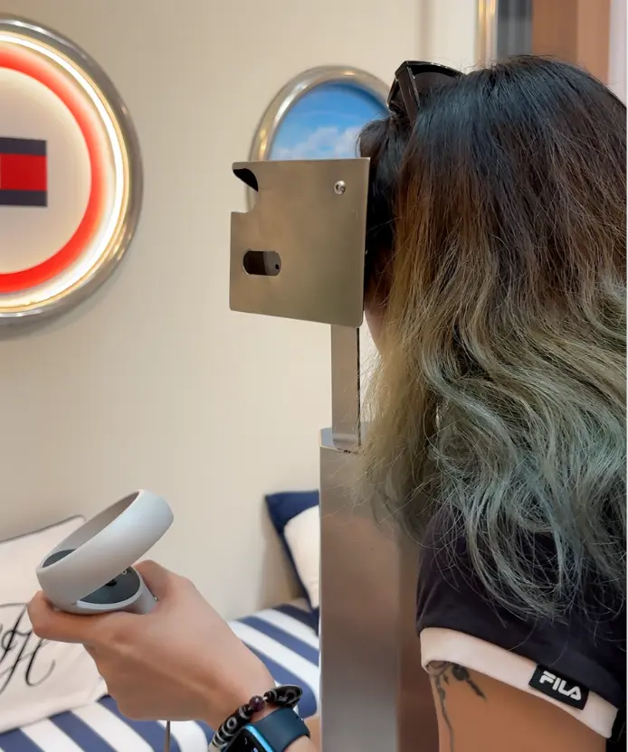 Side view of a woman using the viewfinder while holding a VR controller, Tommy Hilfiger logo behind