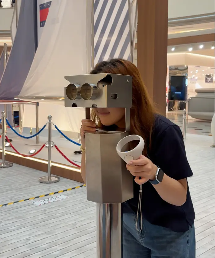 A woman leans into the binocular-style viewfinder in the mall atrium, holding a white VR controller