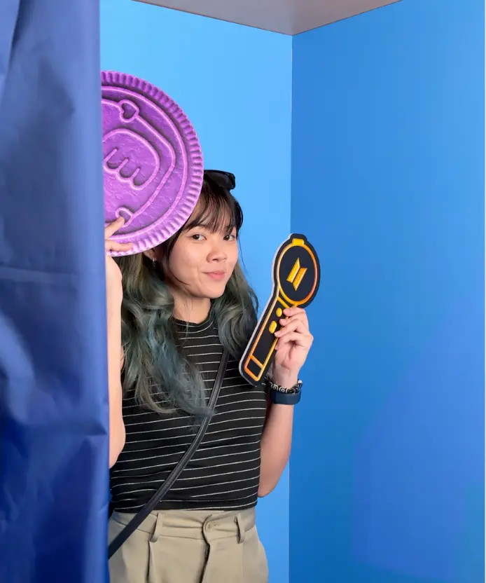 Visitor inside the blue photobooth smiling and posing with a giant purple Oreo cookie prop and a BTS light stick prop