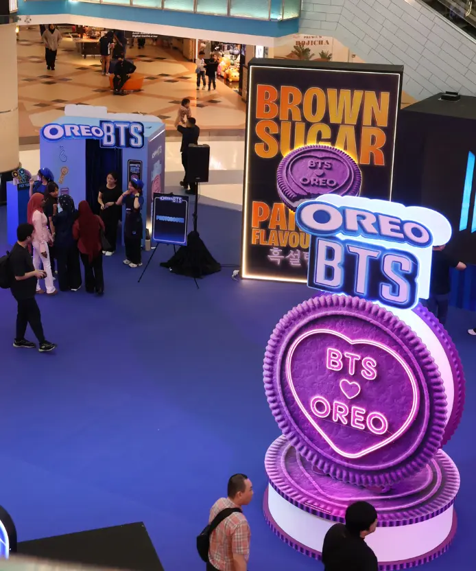 Overhead view of the Oreo BTS event space with visitors queuing at the photobooth, a Brown Sugar flavour digital screen, and a giant purple "BTS Oreo" heart-embossed cookie display