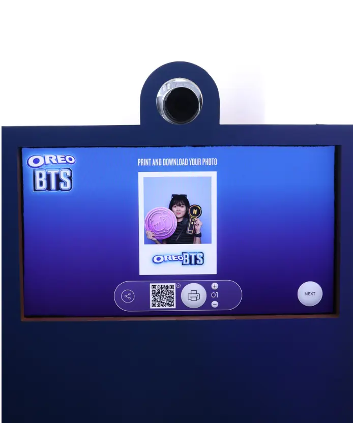 Photobooth touchscreen showing the "Print and Download Your Photo" screen with a QR code, print button, and preview of a visitor's Oreo BTS branded photo