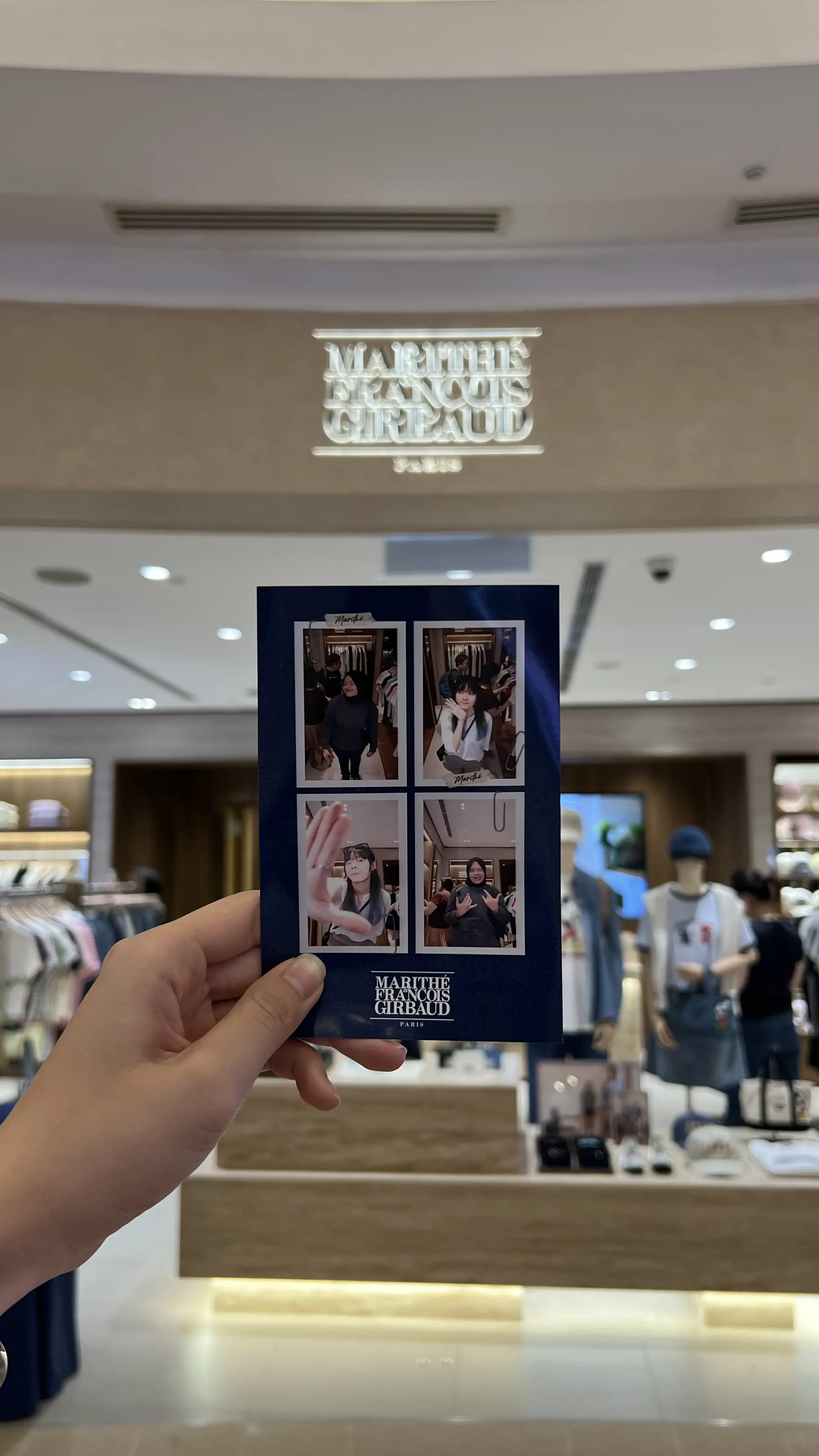 Hand holding a Marithé + François Girbaud photo print in front of the KLCC store signage