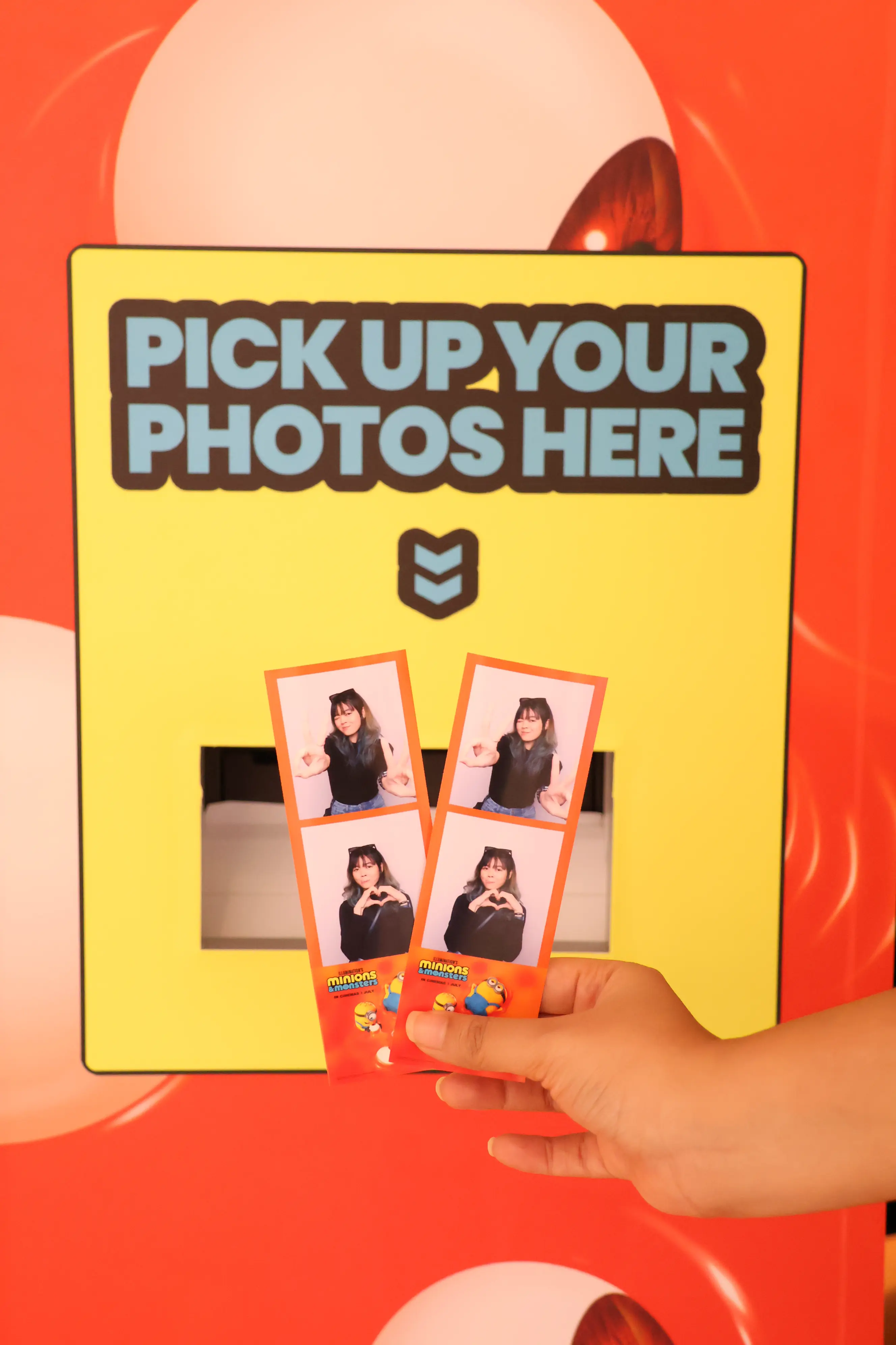 Hand holding two Minions & Monsters photo strips at the pick-up window