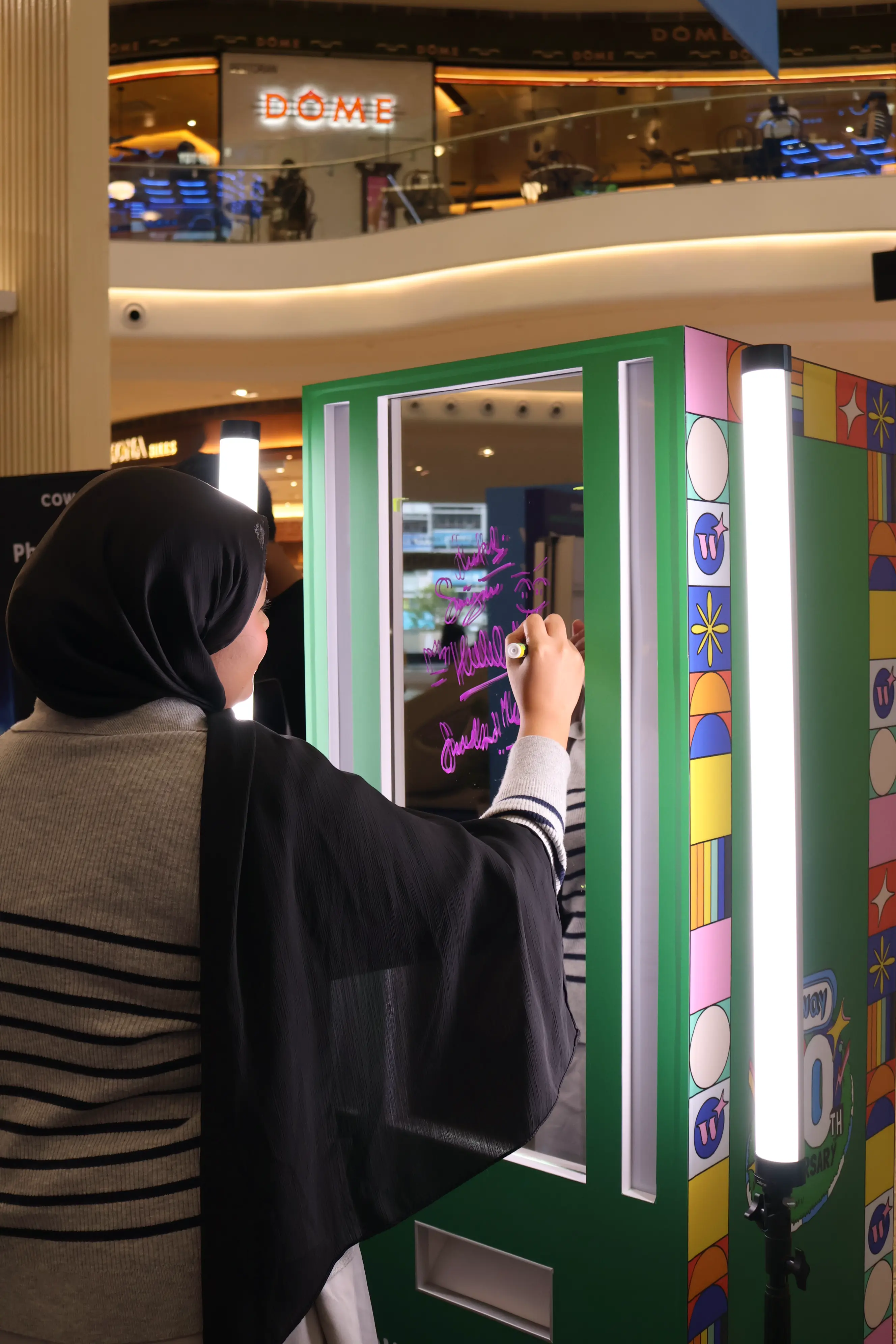 Guest drawing on the Coway booth's illuminated glass with a fluorescent marker