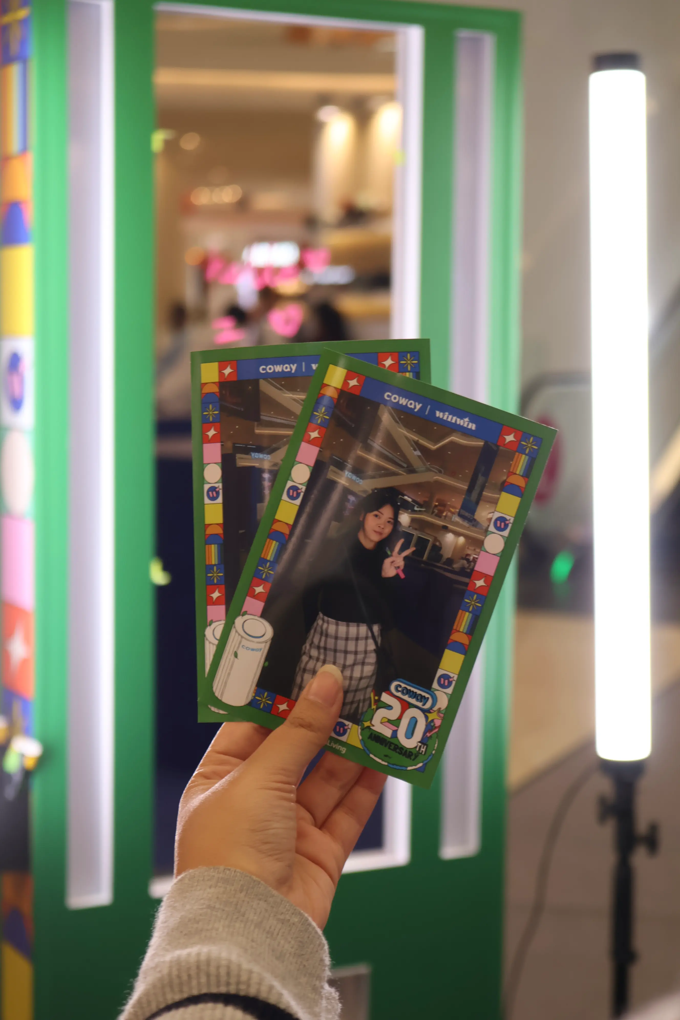 Hand holding two printed Coway 20th anniversary photo cards at the booth