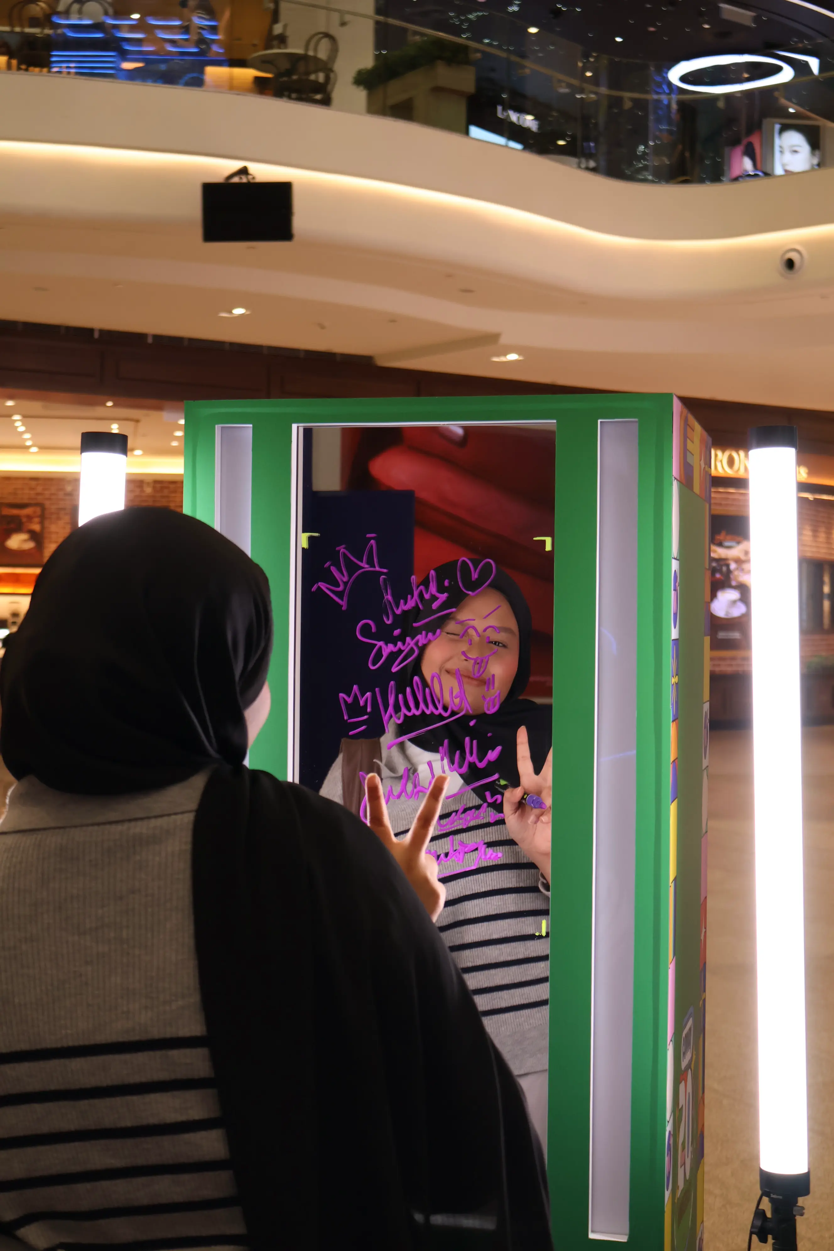 Guest posing with peace signs behind the glass covered in neon doodles