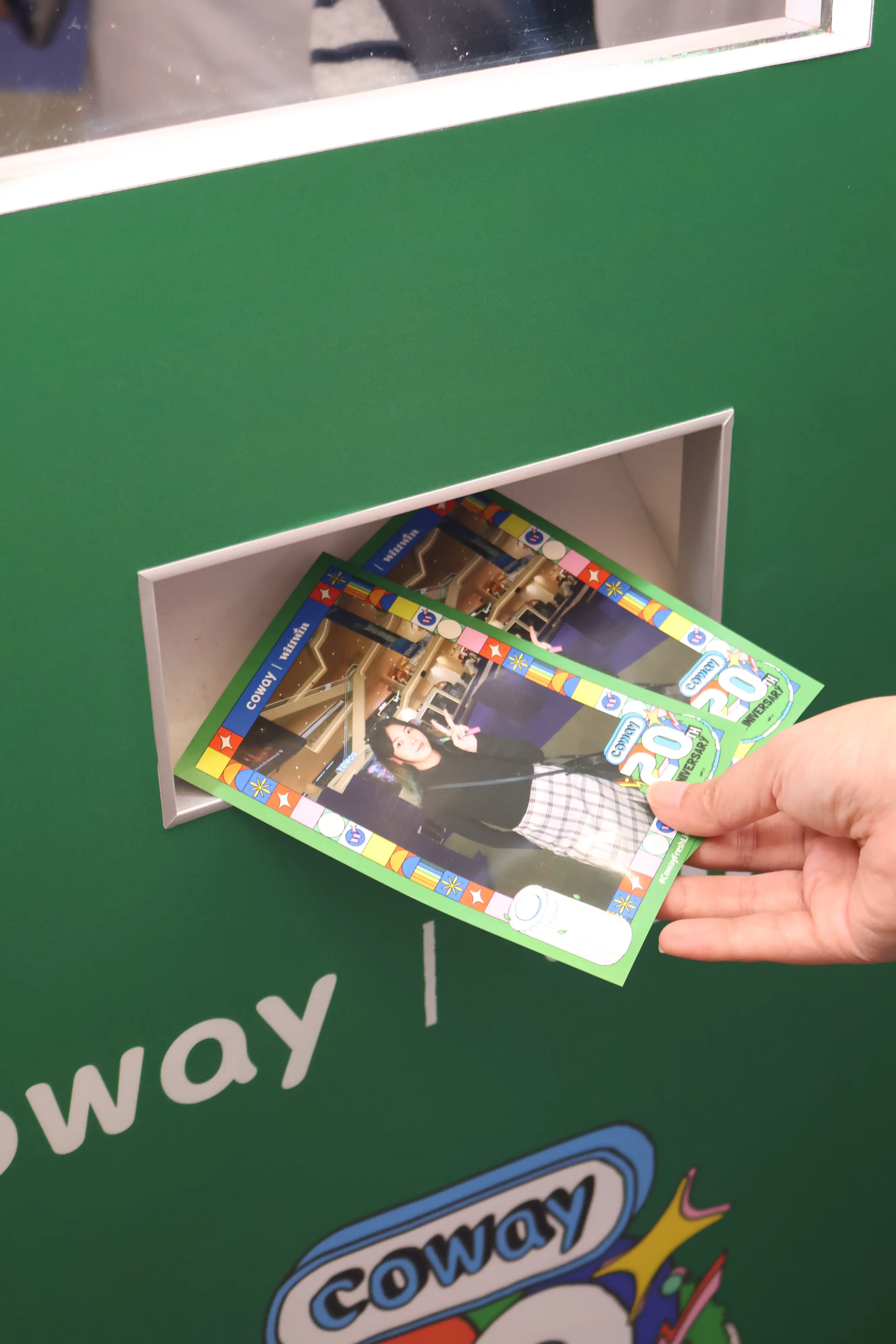 Printed Coway photo cards dispensing from the booth's photo slot