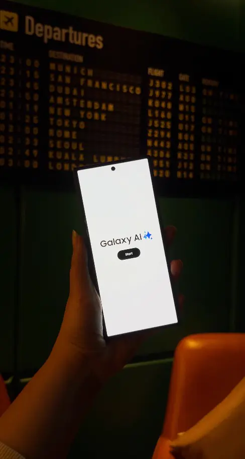 Hand holding a Galaxy AI phone in front of the departures board decor