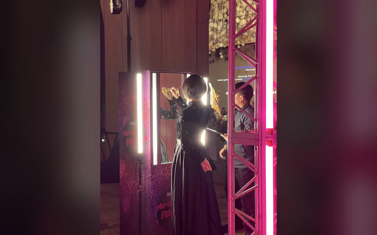 Guest in a black sequinned top writes on the glass booth beside a pink neon truss at the HAYS Year End Party in Kuala Lumpur