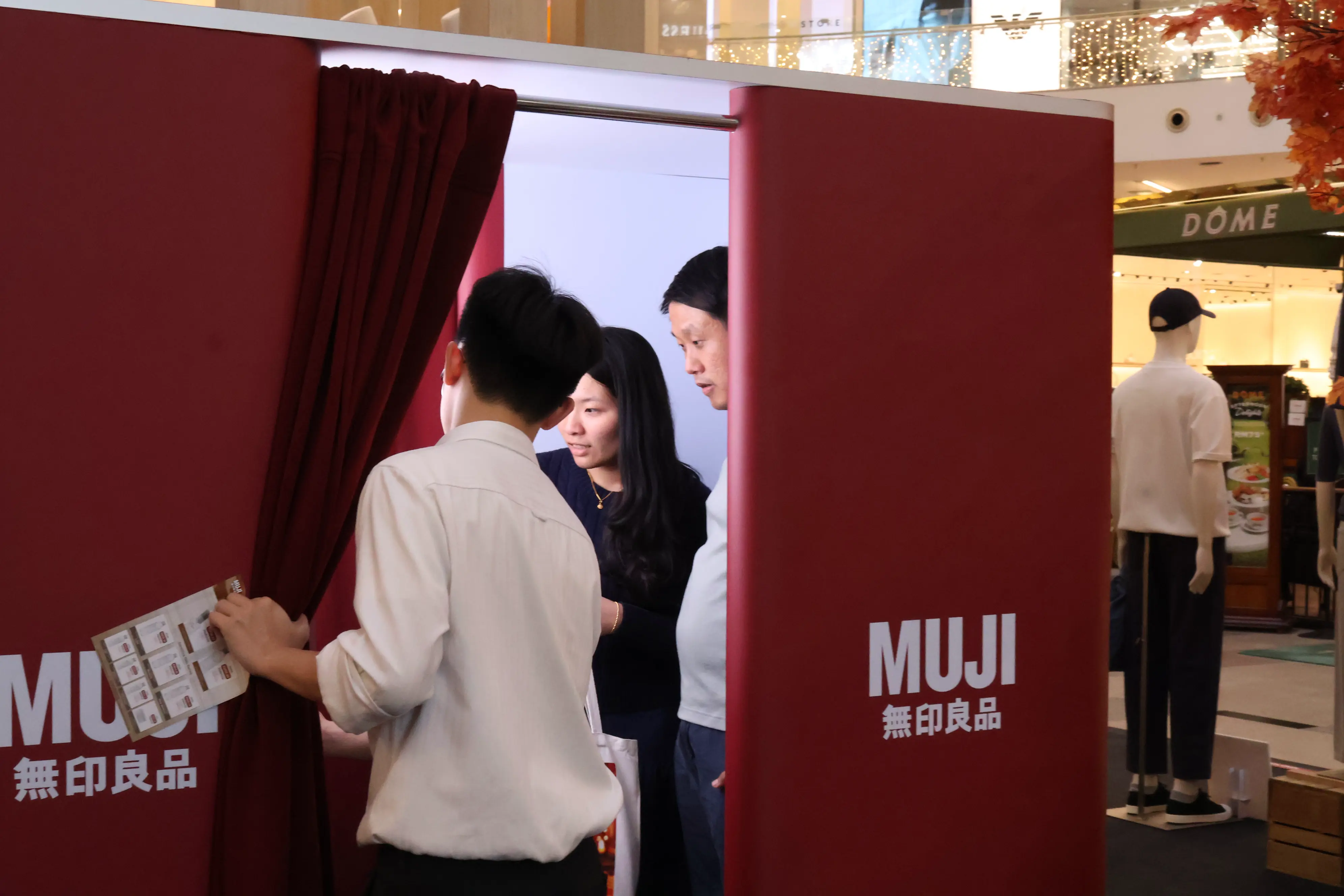 Staff member guiding two shoppers into the red MUJI photo booth