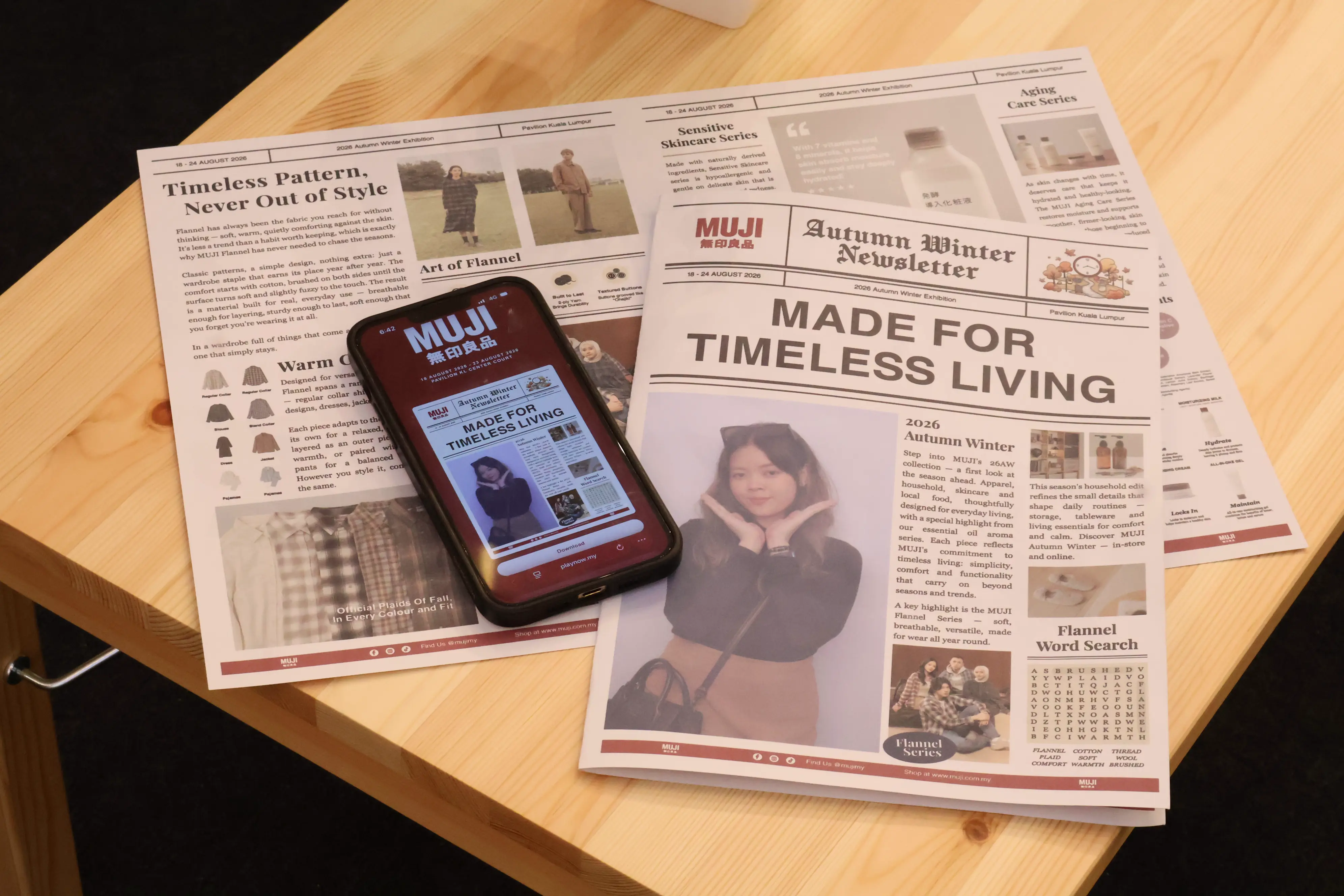 Printed MUJI Autumn Winter Newsletter keepsakes beside a phone showing the digital download