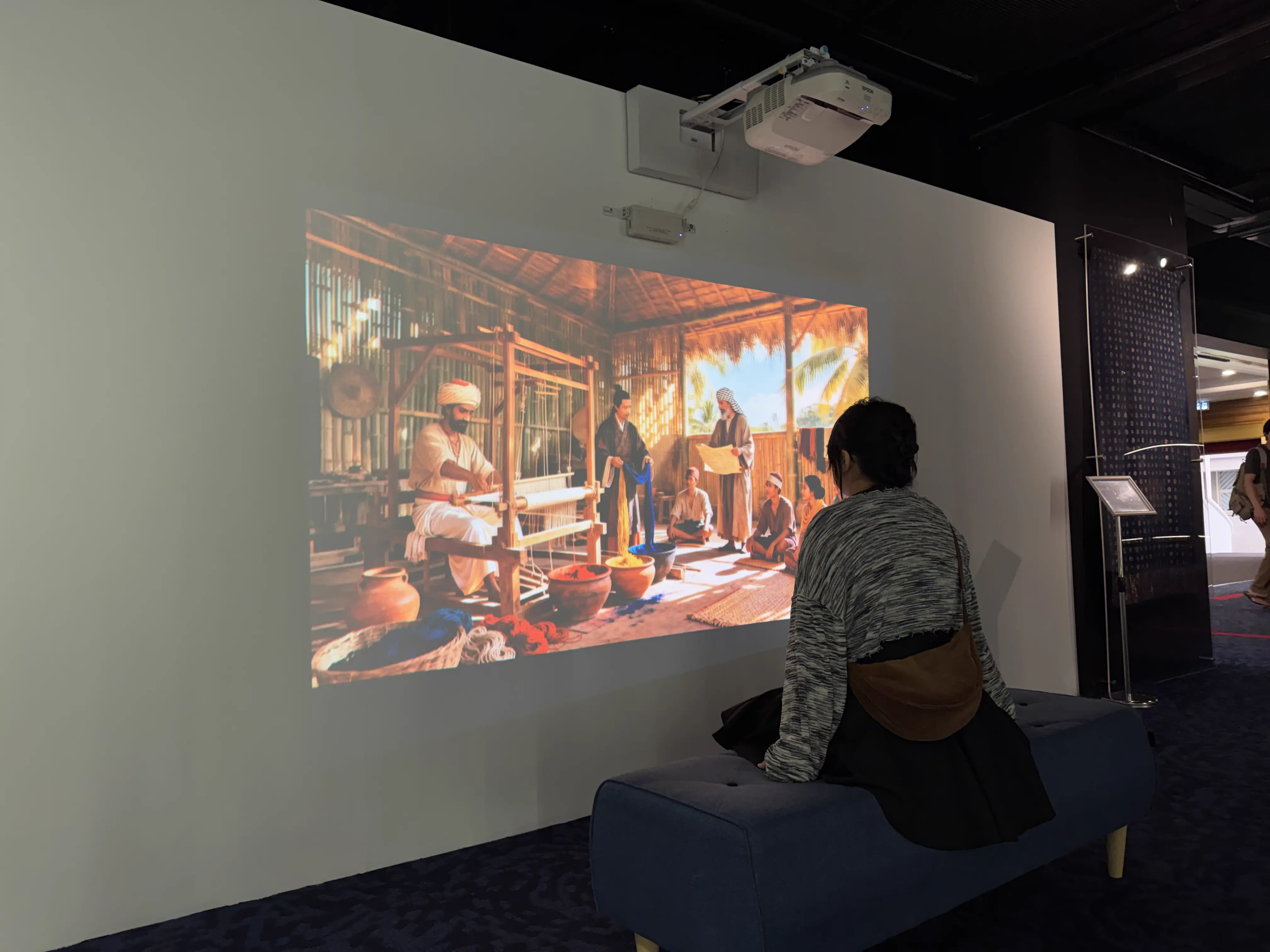 Visitor watching the AI-generated weaving heritage story video projected on the gallery wall