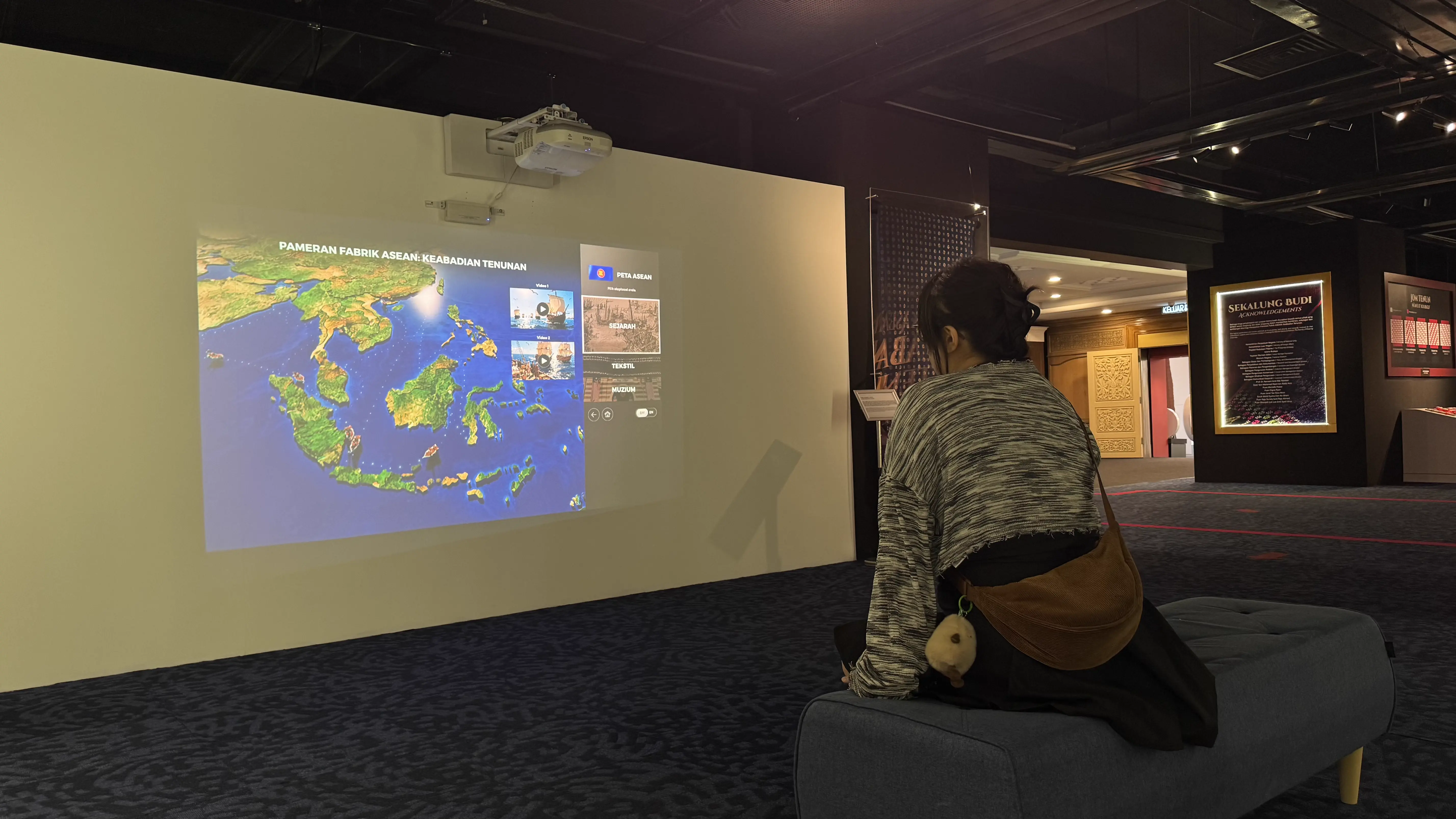 Visitor seated on a bench using the projected Pameran Fabrik ASEAN interactive map
