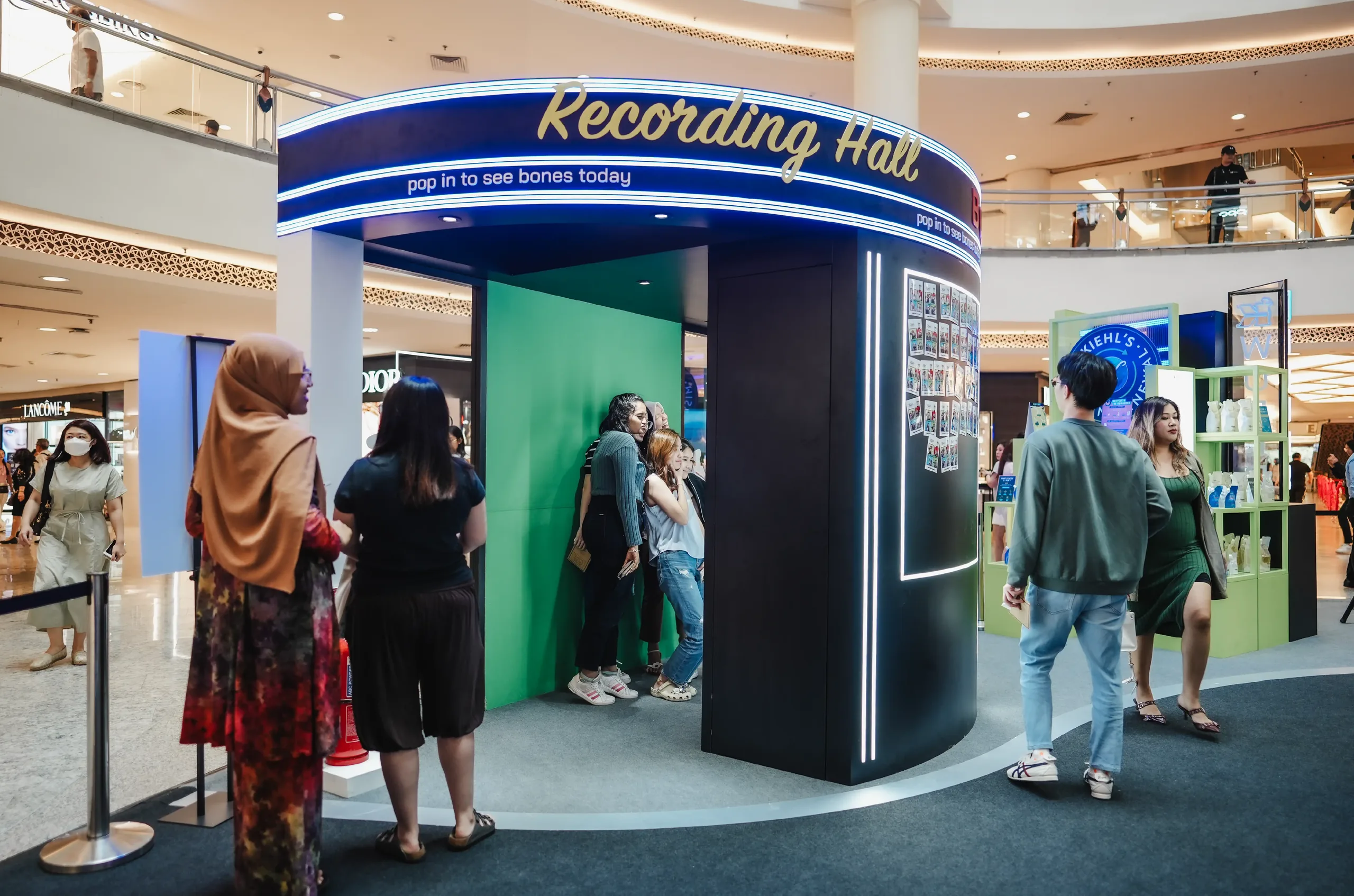 Guests pose inside a green-screen 'Recording Hall' photo booth in a shopping mall.