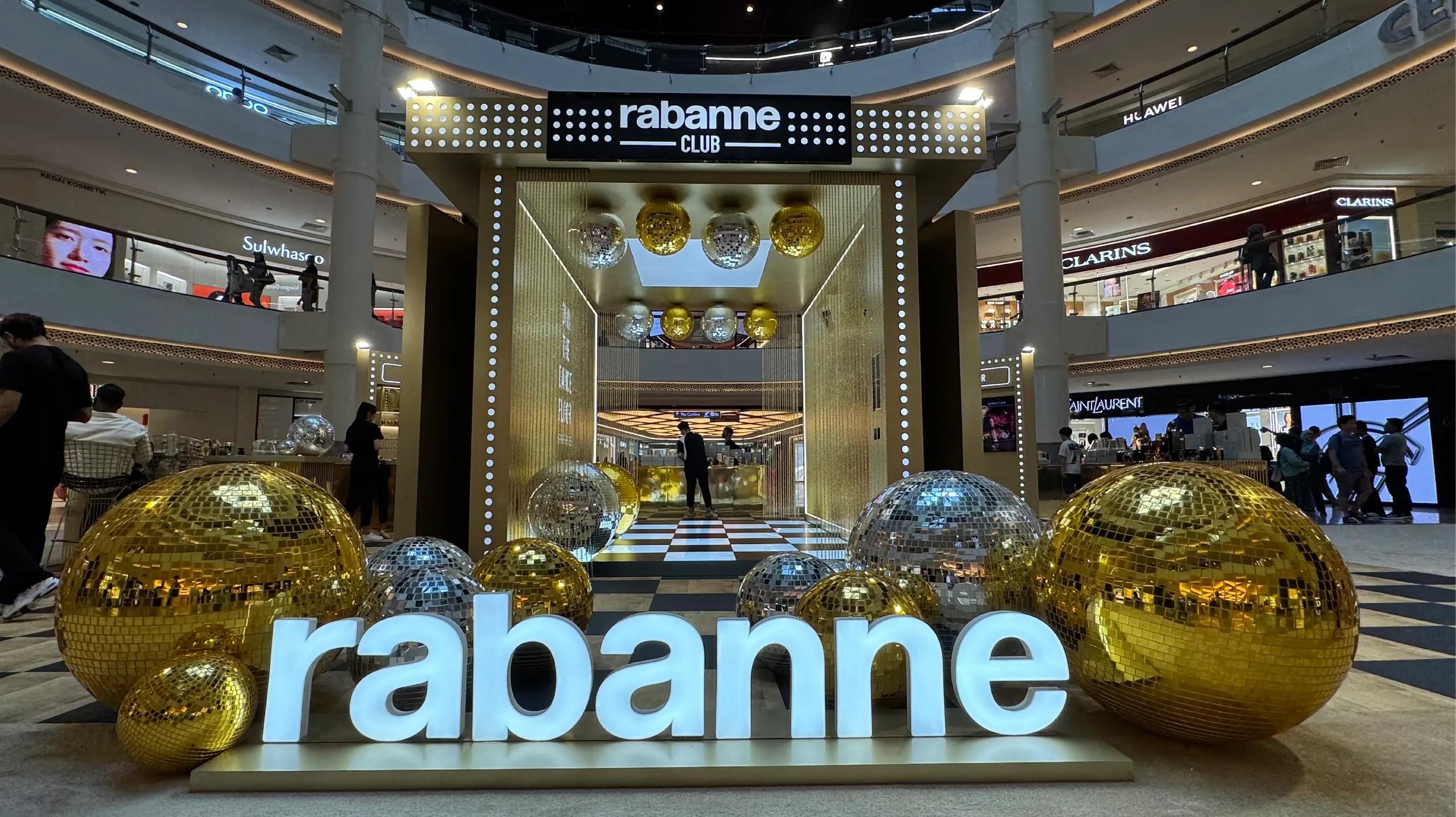 A branded 'Club' entrance decorated with gold and silver disco balls in a shopping mall atrium.