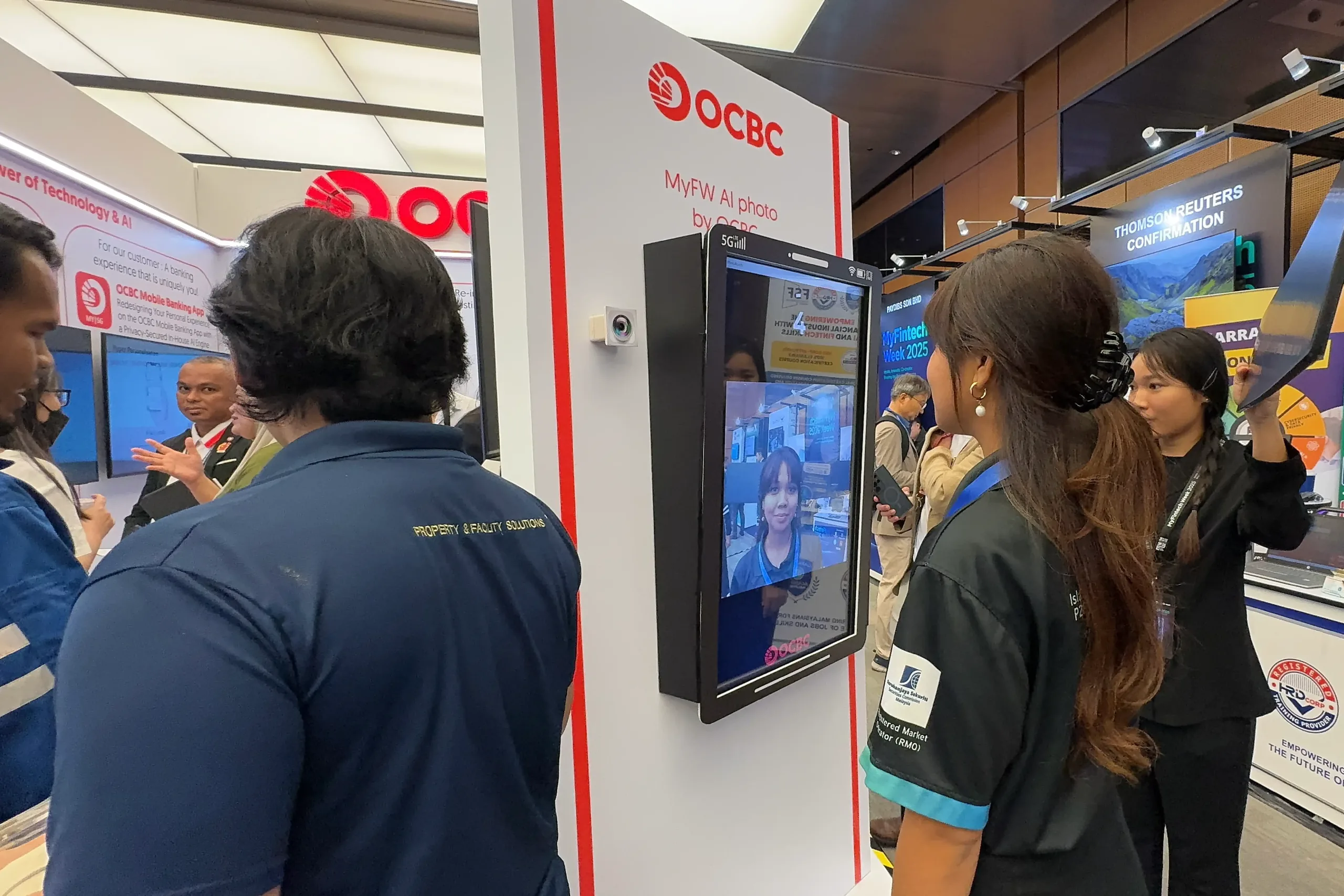 A woman has her photo taken at a branded AI photo kiosk as others watch.