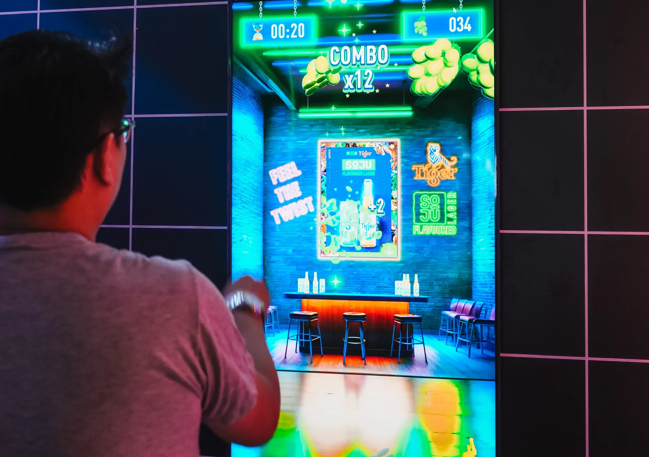 A man plays a neon-lit motion-game screen with combo scoring and beverage-branded artwork inside a bar scene.