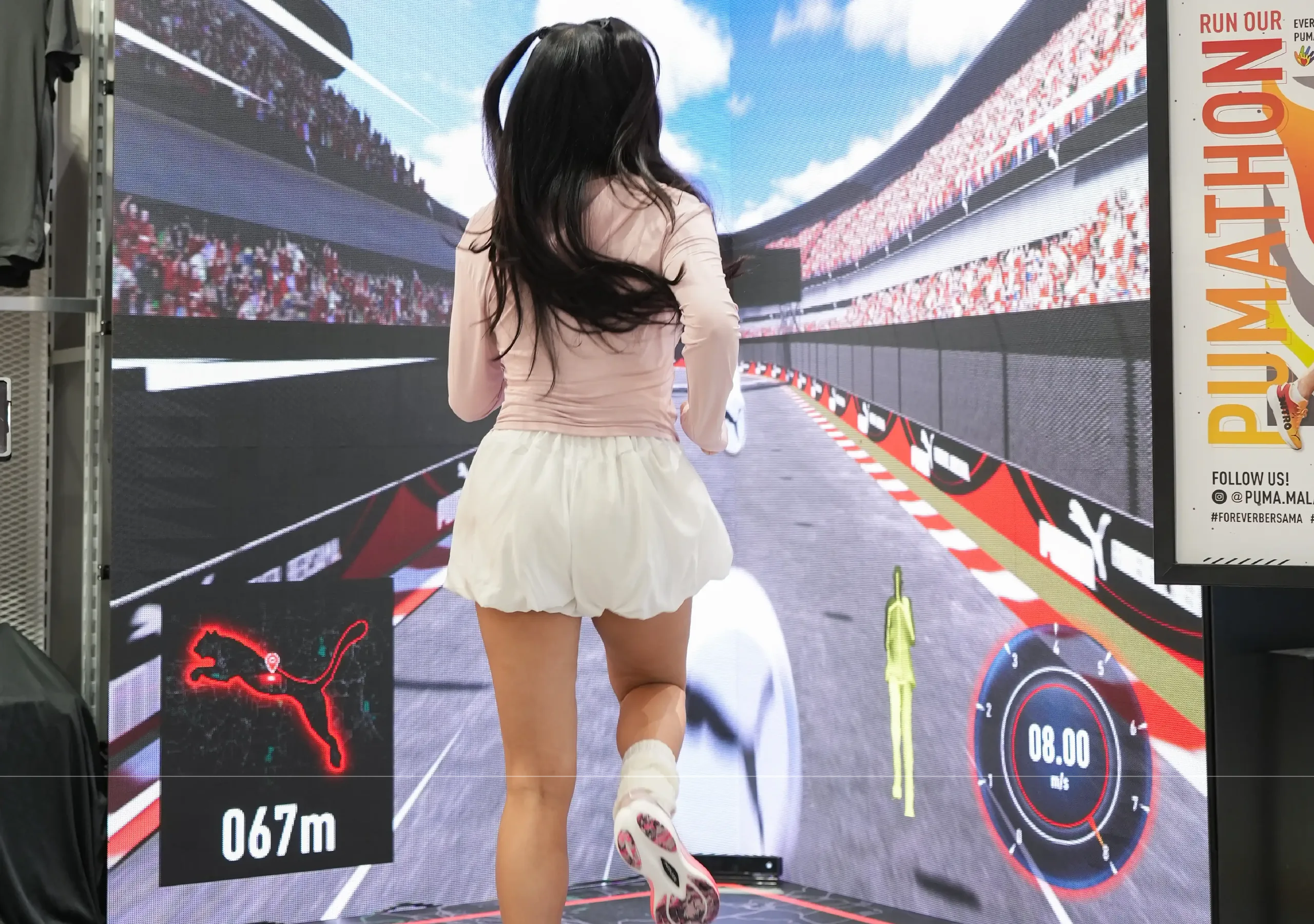 A woman runs in place on a digital racetrack treadmill screen showing her distance and pace.