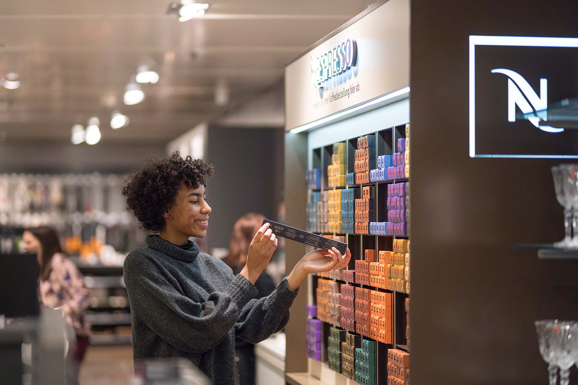Frau steht neben einem Nespresso-Kaffeestand in einem Nespresso-Shop