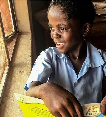 A young girl smiles while reading a book.