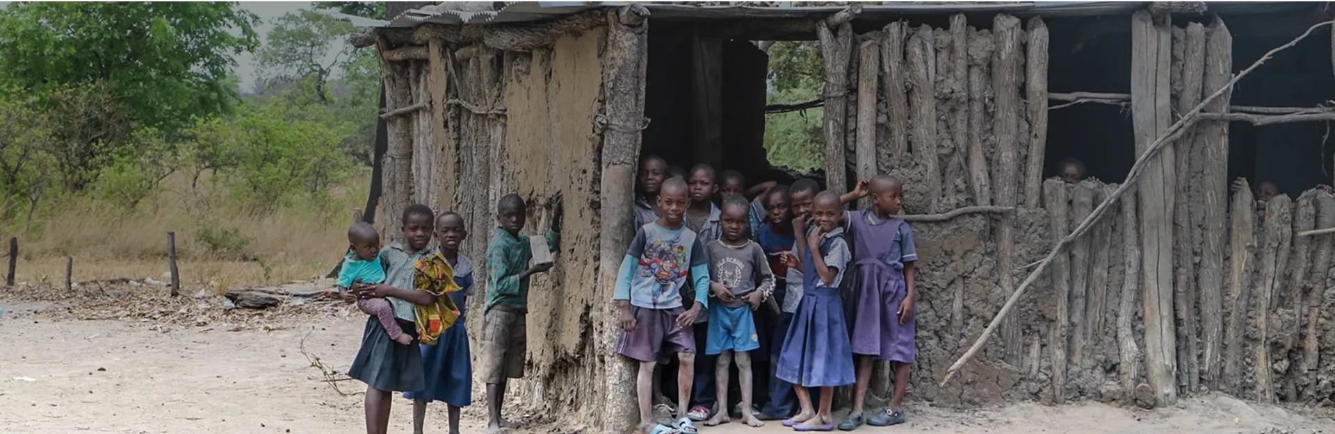 A group of children standing in front of a hut.