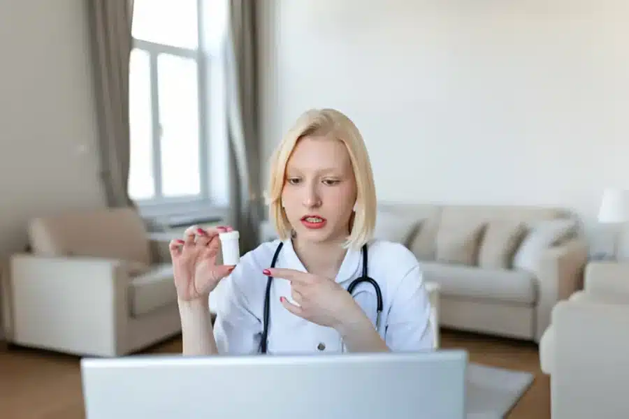 A woman in a white coat sits at a table with a laptop, engaged in a consulting session.