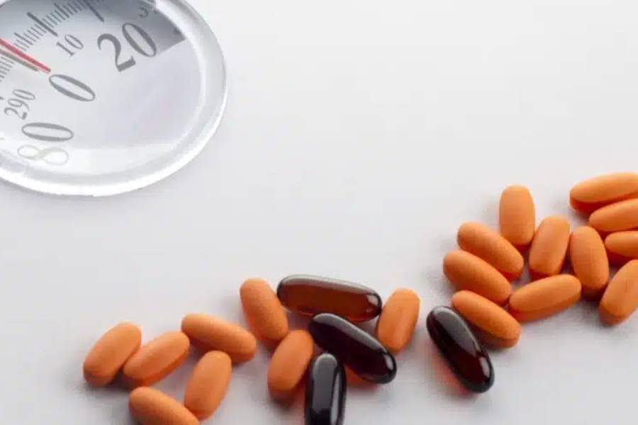 A thermometer and weight loss pills arranged on a white surface, indicating health monitoring and medication.