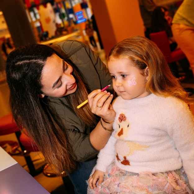 A group of five people posing in a colorful party store, wearing oversized sunglasses and holding balloons. The background features shelves filled with party supplies and colorful decorations.