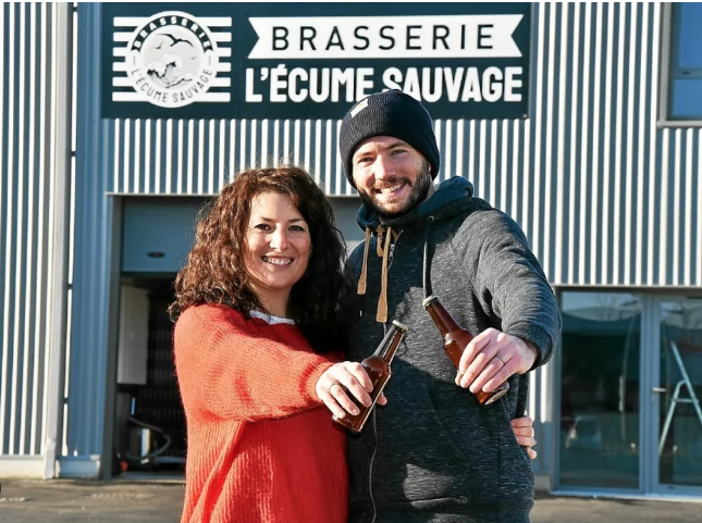 Image principale : Deux personnes souriantes posant derrière un comptoir avec des bouteilles de bière devant un logo de brasserie. Elles semblent fières de présenter leurs produits, dans un cadre professionnel et accueillant. Image miniature : Deux personnes souriantes se tiennent devant l'entrée d'une brasserie nommée 'Brasserie L'Écume Sauvage'. L'une d'elles tient une bouteille de bière dans chaque main, et ils posent devant un panneau avec le logo de la brasserie.