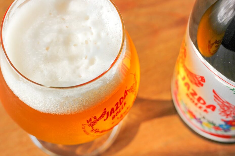 Verre de bière artisanale Jazda Bolek avec un logo rouge distinctif, accompagné d'une bouteille décorée de motifs floraux, illustrant l'ambiance conviviale de L'instant bière