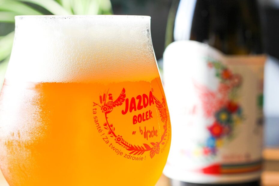 Verre de bière artisanale Jazda Bolek avec un logo rouge distinctif, accompagné d'une bouteille décorée de motifs floraux, illustrant l'ambiance conviviale de L'instant bière