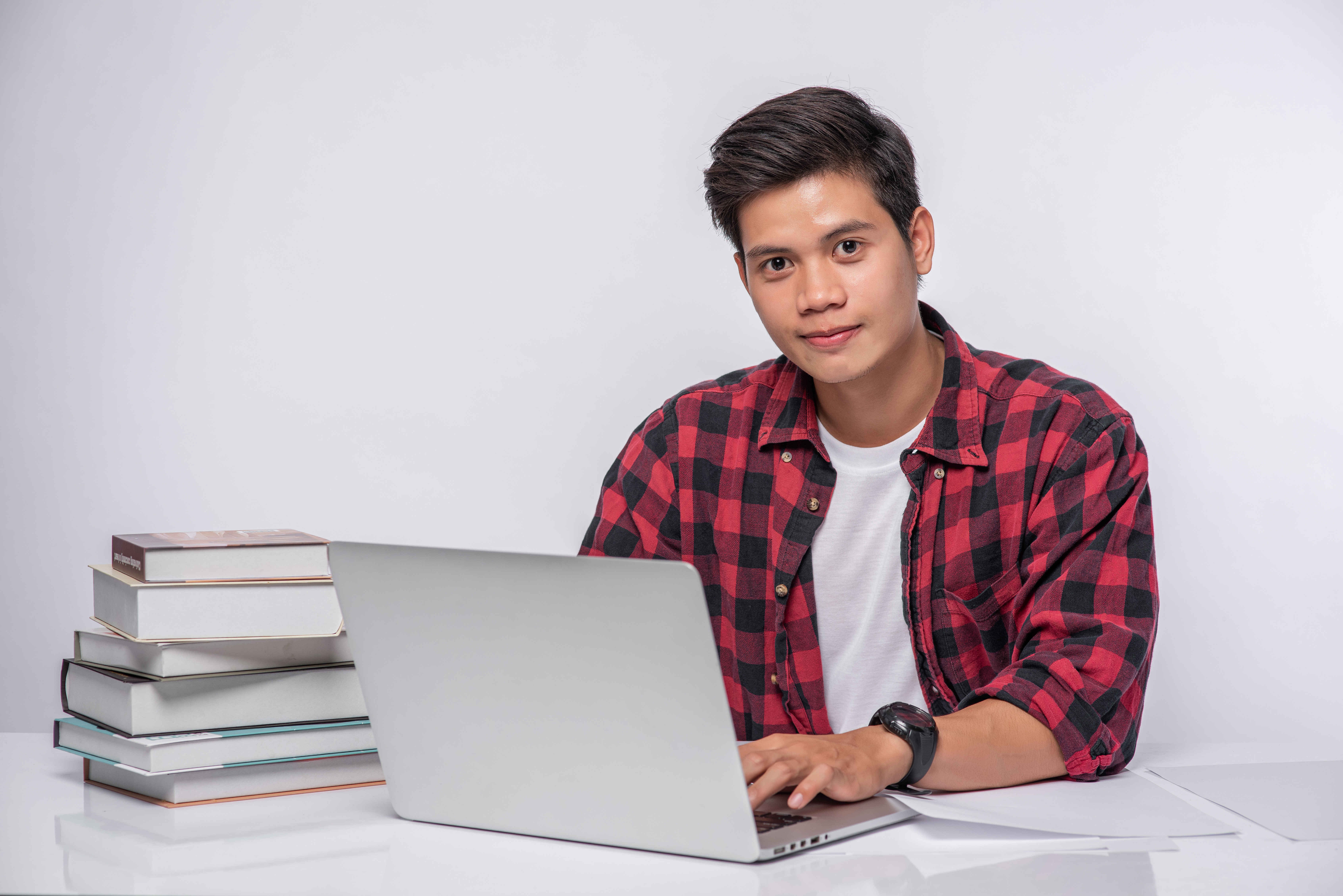 A young man using a laptop, looking at the camera with a subtle, discreet smile.