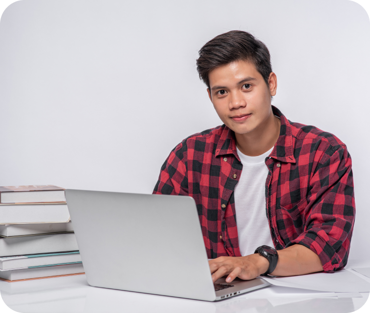 A young man using a laptop, looking at the camera with a subtle, discreet smile.