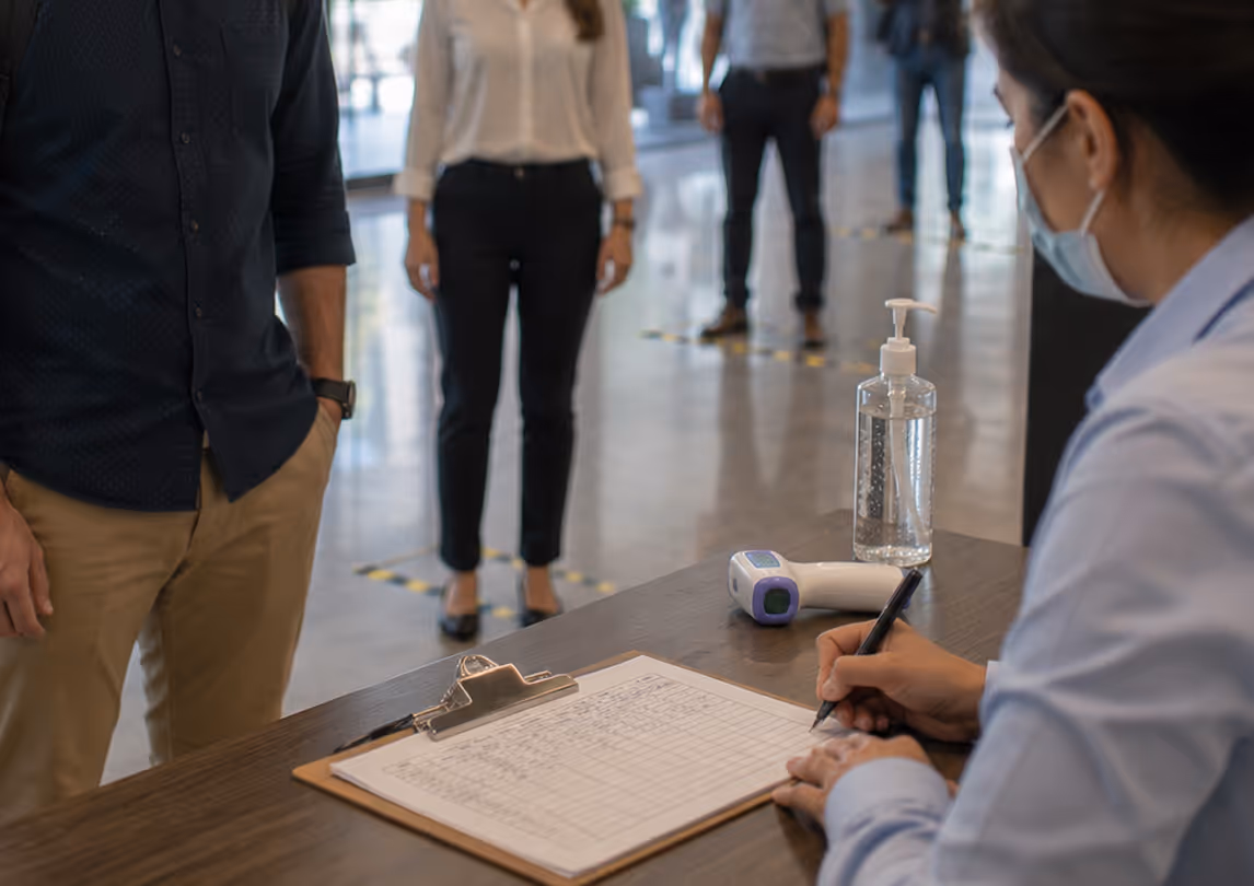 Manual workplace health screening process with paper forms, thermometer, and sanitizer showing slow tracking before automation.