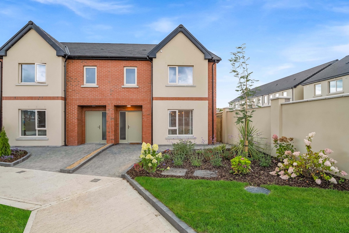 Modern semi-detached house with brick center, beige sides, green doors, garden, and paved driveway.