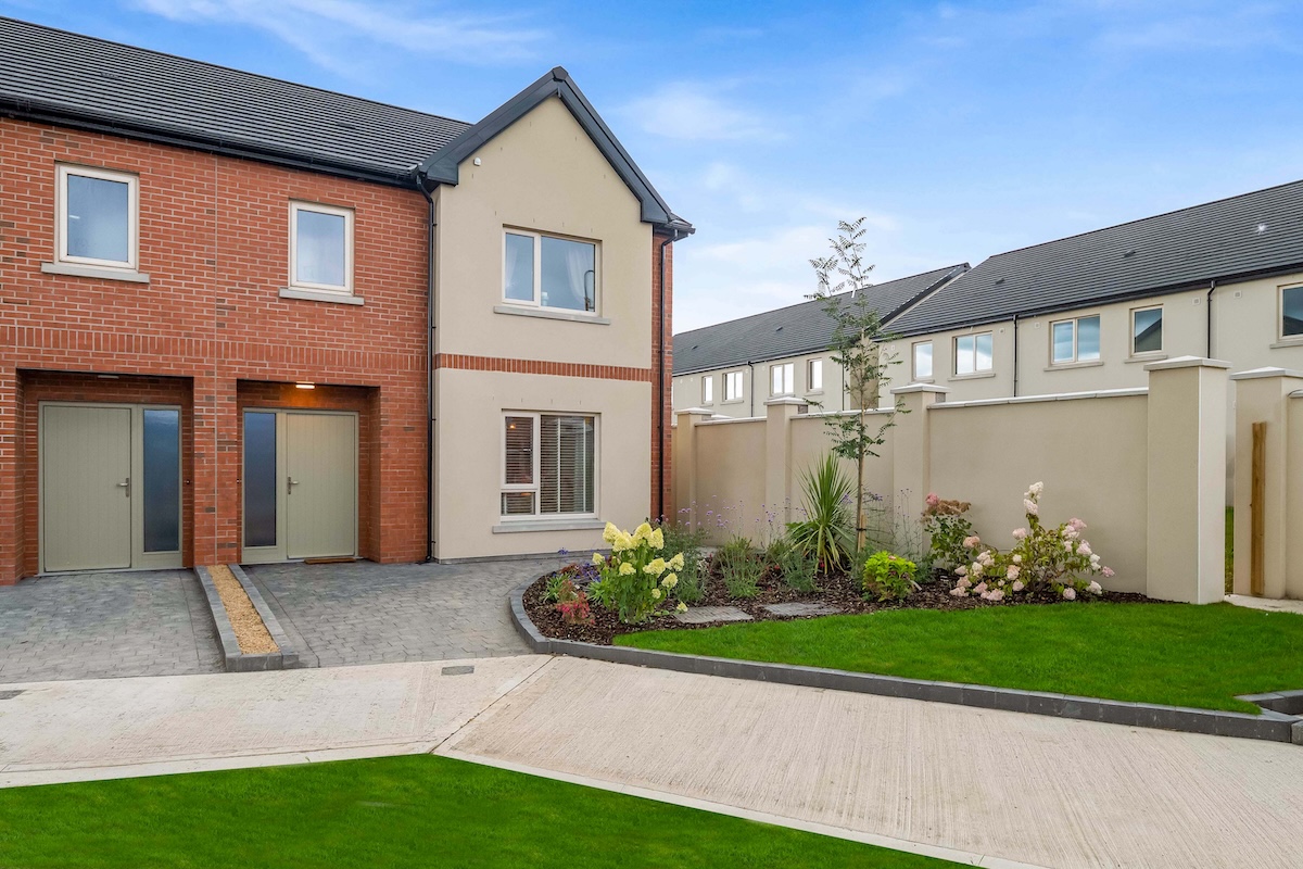 Modern two-story townhouses with brick and beige facades, paved driveways, and a landscaped garden.