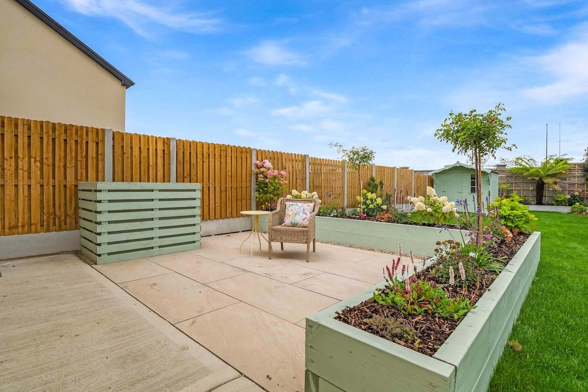 Backyard with raised garden beds, a wooden fence, a chair with floral cushion, and a small green shed.