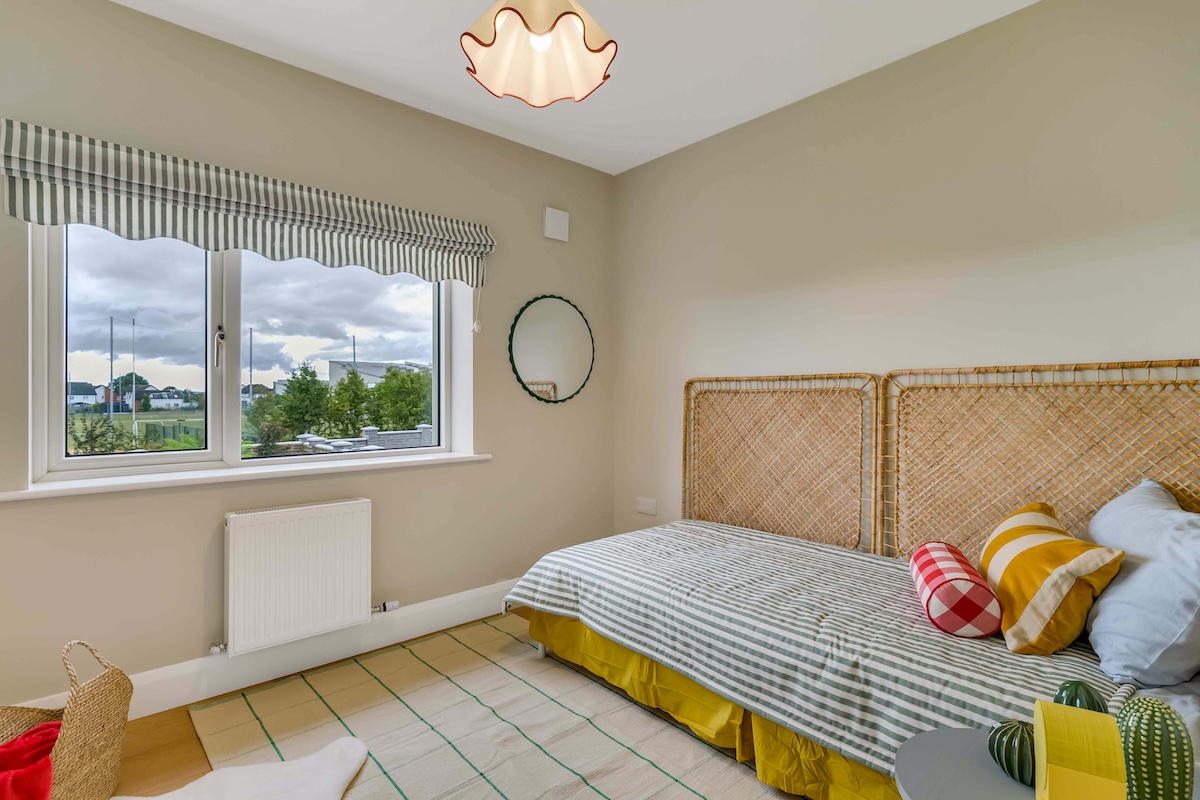 Bedroom with a single bed with striped bedding, wicker headboards, colorful pillows, and a window with striped valance.