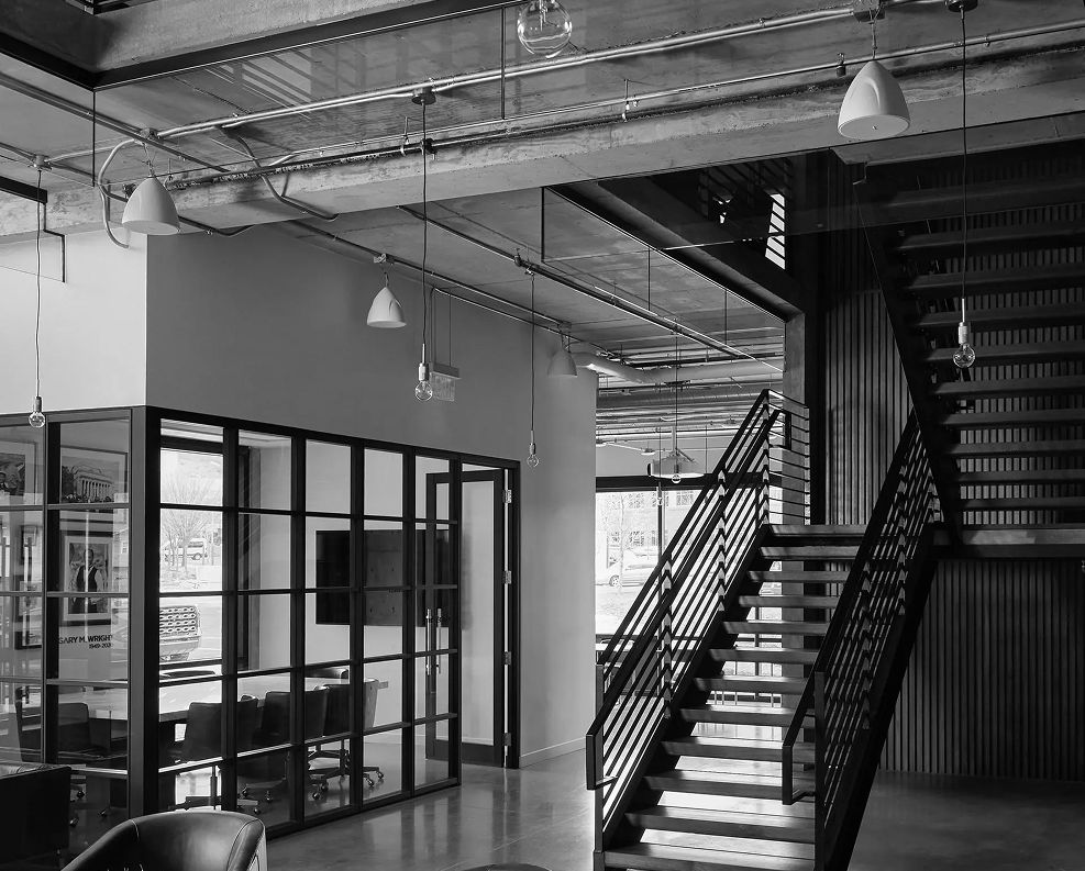 Industrial-style interior featuring an open staircase and glass-walled meeting rooms, showcasing a modern office environment with exposed ceilings and sleek finishes