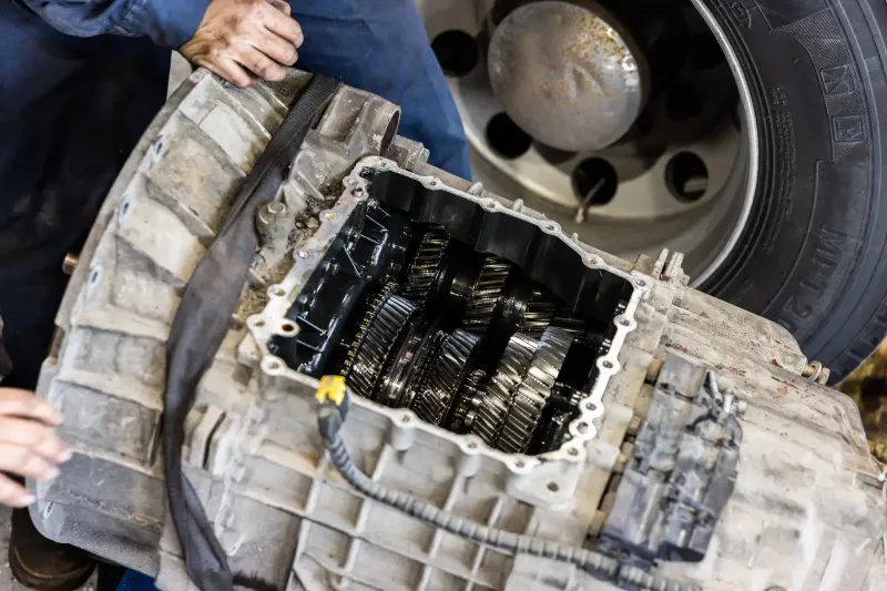Heavy-duty transmission repair with exposed gears during inspection beside a truck wheel.