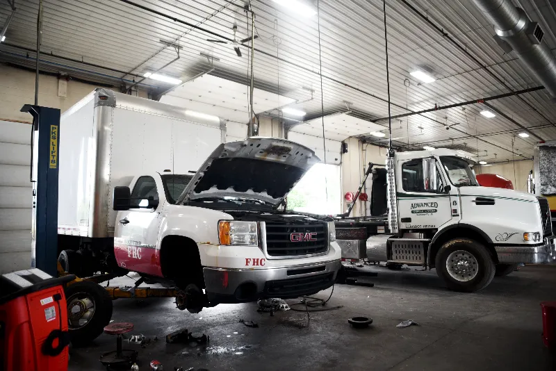 GMC FHC box truck on lift for heavy-duty truck repair beside an ADVANCED tow truck.